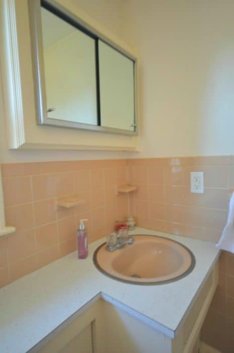 A pink sink in a bathroom with pink tiles halfway up, and a medicine cabinet with sliding mirror doors