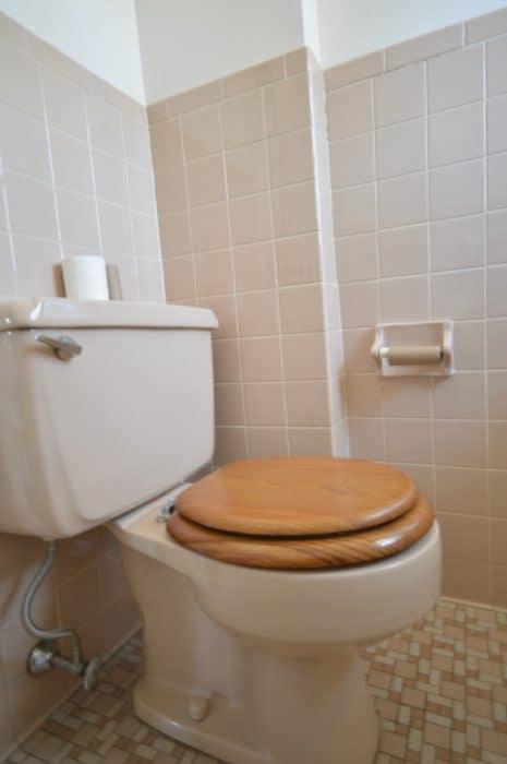 A pink toilet with wooden seat and large, square pink tiles on the wall