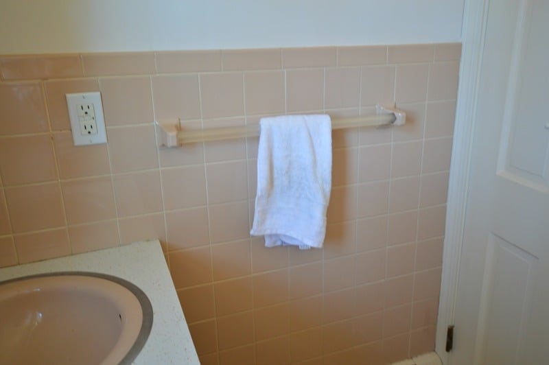 A bathroom wall with pink tiles halfway up, and a pink towel rack holding a white towel