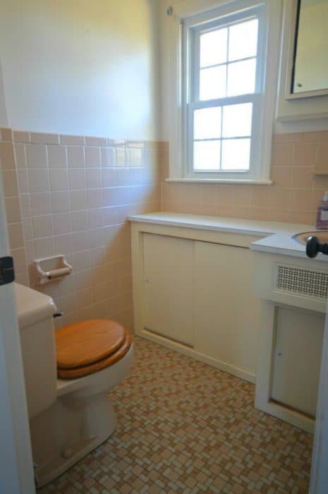 A bathroom with pink tiles halfway up the wall, a wooden cupboard under the window, and small orange and brown tiles on the floor