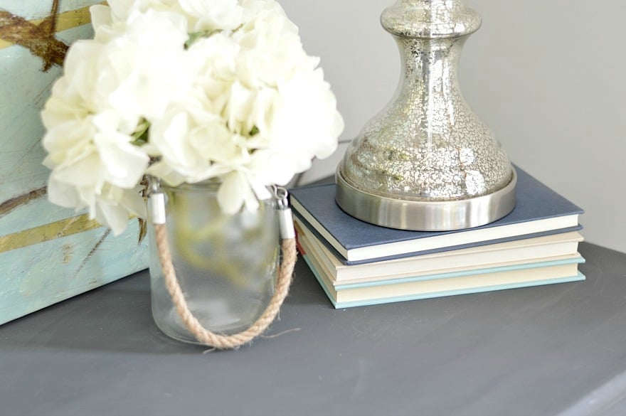 The base of silver lamp shade on top of a stack of books, next to a small vase of white flowers