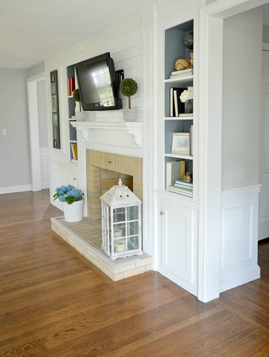 A fireplace with a flat-screen television, built-in side shelves and a hearth with a large lantern