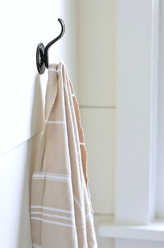 A tan hand towel on a dark, metal towel hook, mounted onto shiplap walls