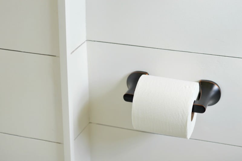 A new roll of toilet paper on black, metal hardware mounted onto shiplap wood plank