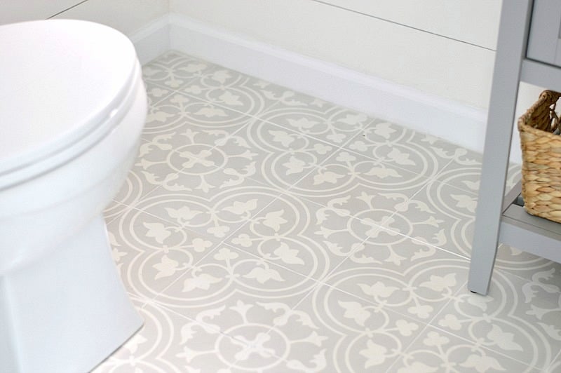Shiplap walls meet white wood trim and a grey and white floral tile floor, near a toilet (wooden seat is gone!)