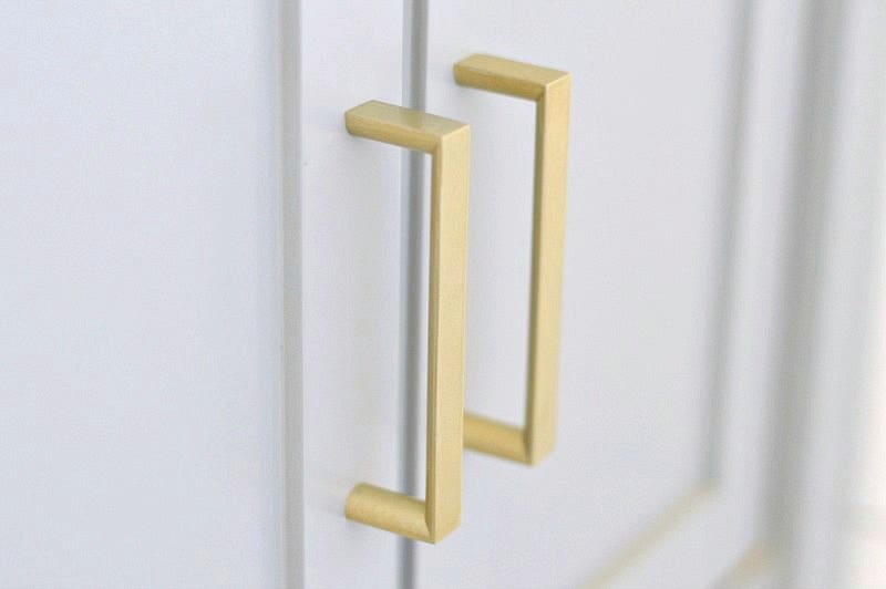 A close up of simple, antique gold handles on the vanity in a bathroom