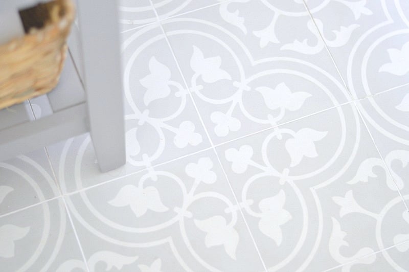 Grey and white tiles on a floor underneath the wooden feet of a grey vanity