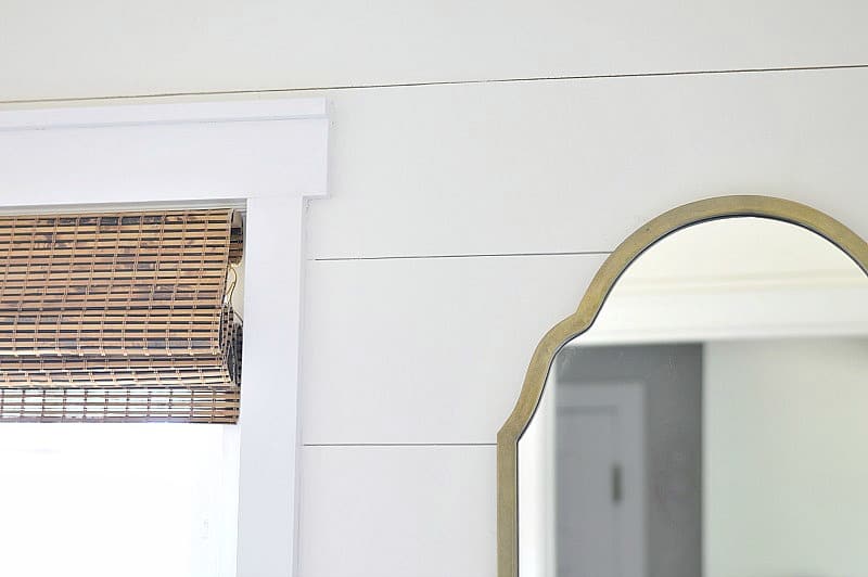 Shiplap wooden walls, a large antique gold framed mirror and wooden blinds in a window