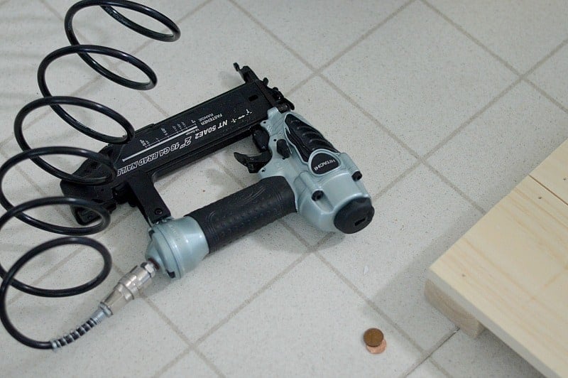 A nail gun on a tile floor, next to wood planks and pennies
