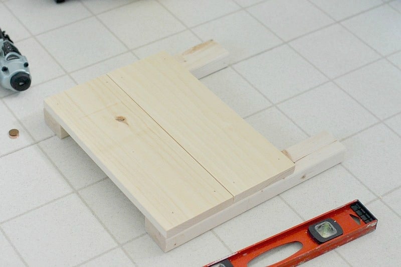Two planks nailed onto a frame to form the first side of a box planter, with a level nearby 