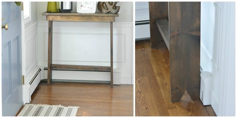 A narrow, wooden hallway table with various decor on top and a notch in the lower sides 