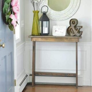 Wooden console table in entryway holding vase, lantern and picture frame