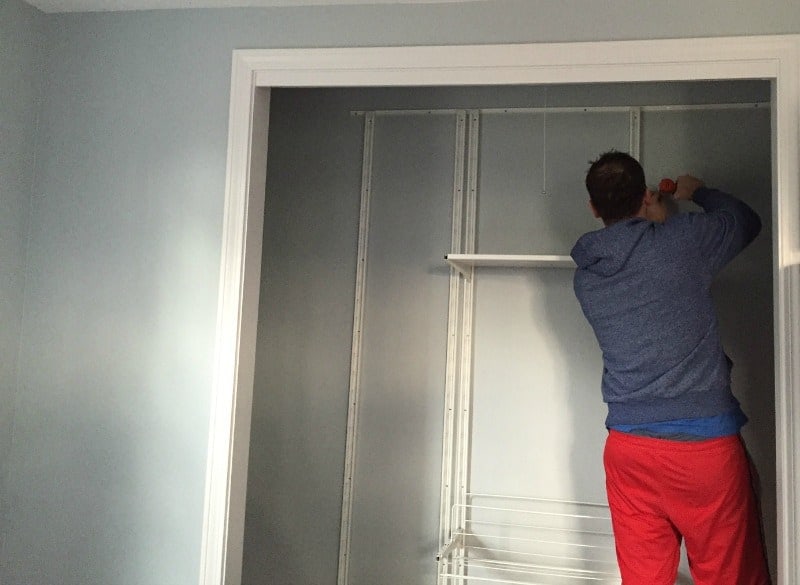 A person in a closet, installing shelves and framework for a closet system