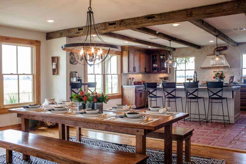 A kitchen and dining room with wood beam ceilings, dark wood cabinets and wood trim, and a wooden table and benches under a rustic chandelier