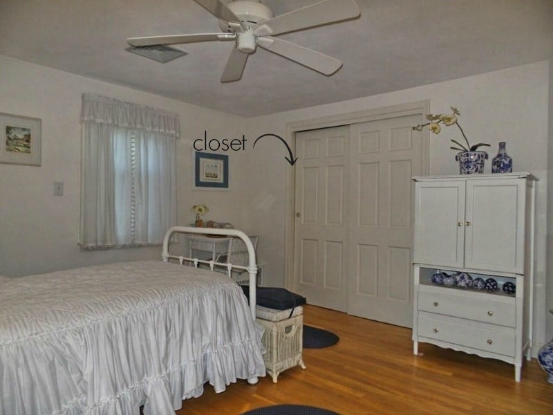 A bedroom with an old-fashioned iron bed, white wardrobe, wooden floors and a closet with white sliding doors