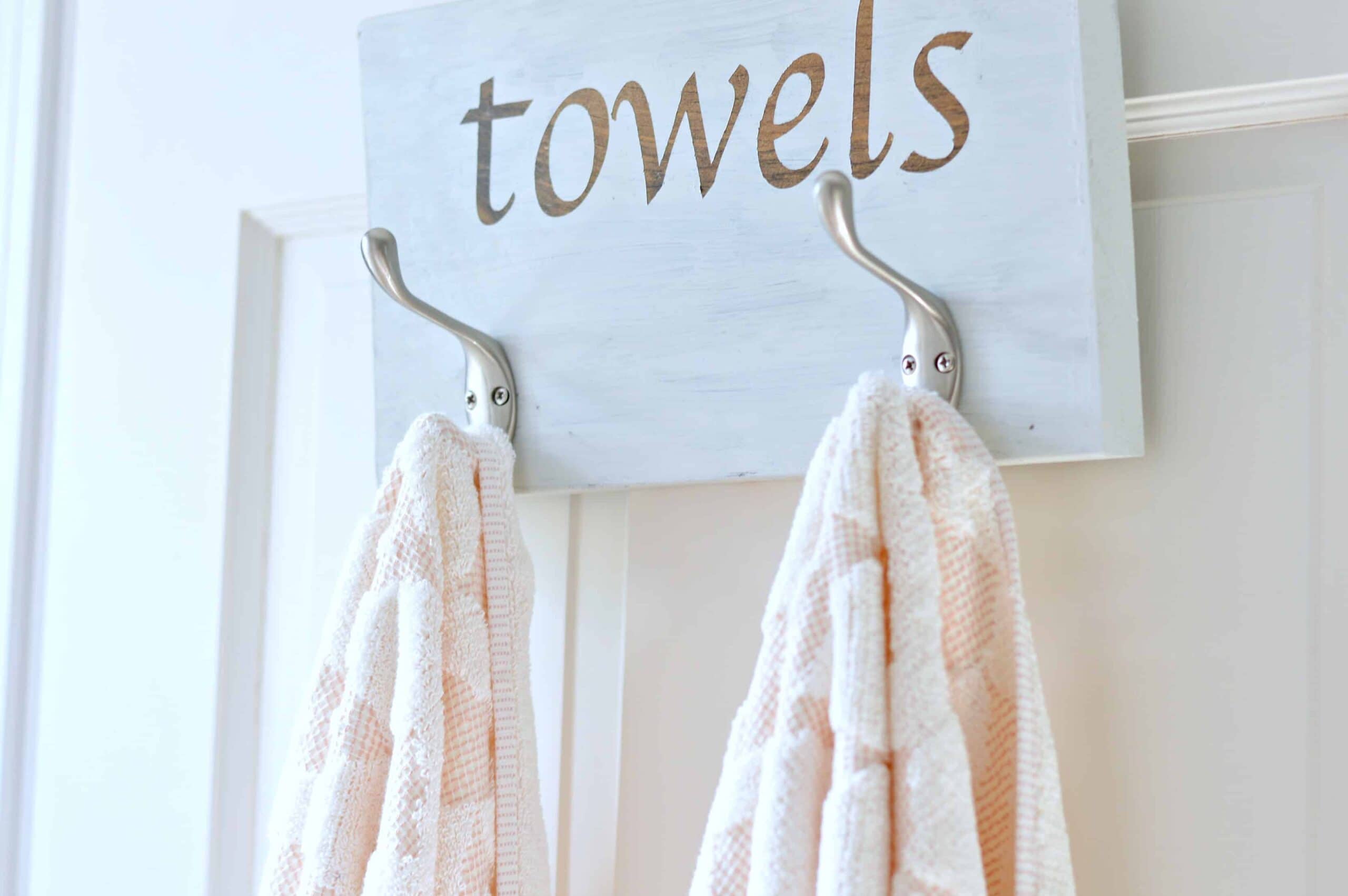 2 towels hung on metal hooks on painted wooden plank, with the word 'towels' in decal sticker