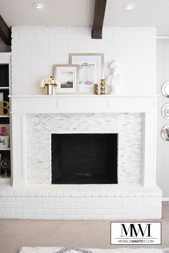 A close up of the fire place with grey and white tile surround, painted white brick hearth and photo frames and decor on top of the mantel