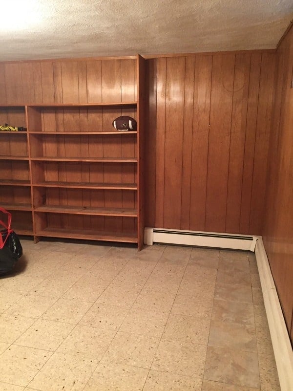 A corner of the basement with wood paneled walls, old tile floors, and a built-in wood shelving system