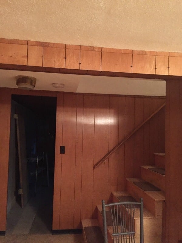 Wood paneled walls, the bottom of a staircase and a door leading to another section of the basement