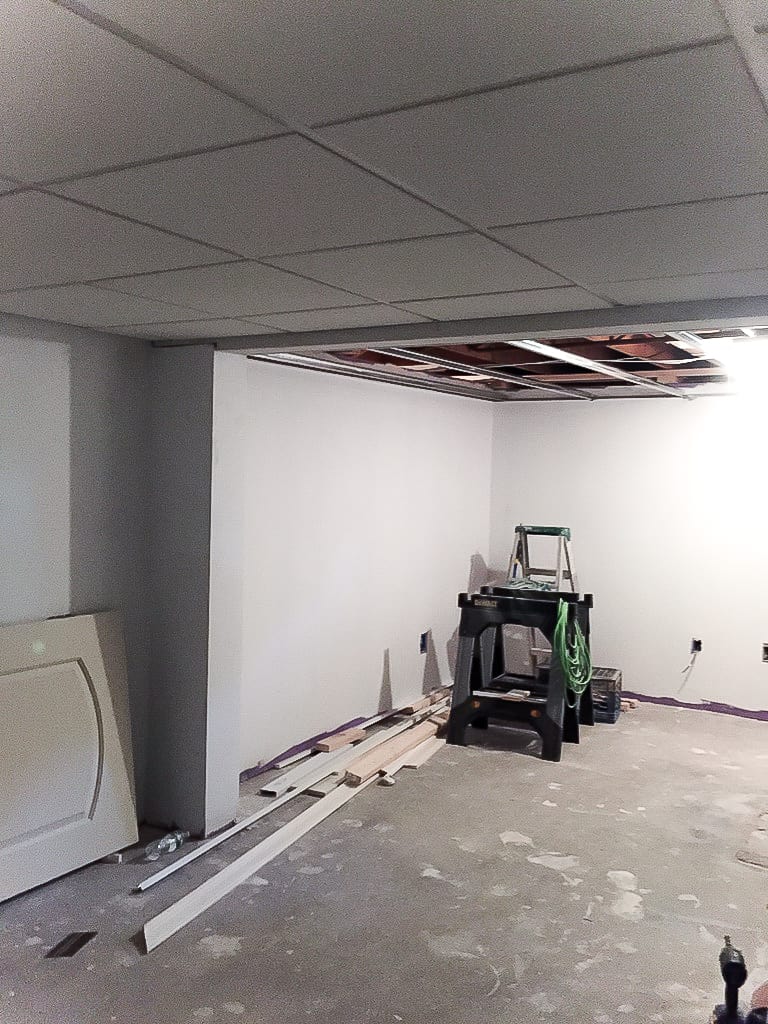 A corner of the basement with renovation materials and a low, drop ceiling with sheets missing from the top