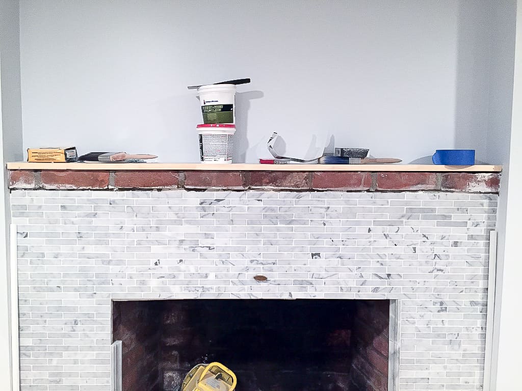 A close up of the top of a fire place with a wooden mantel holding renovation supplies 