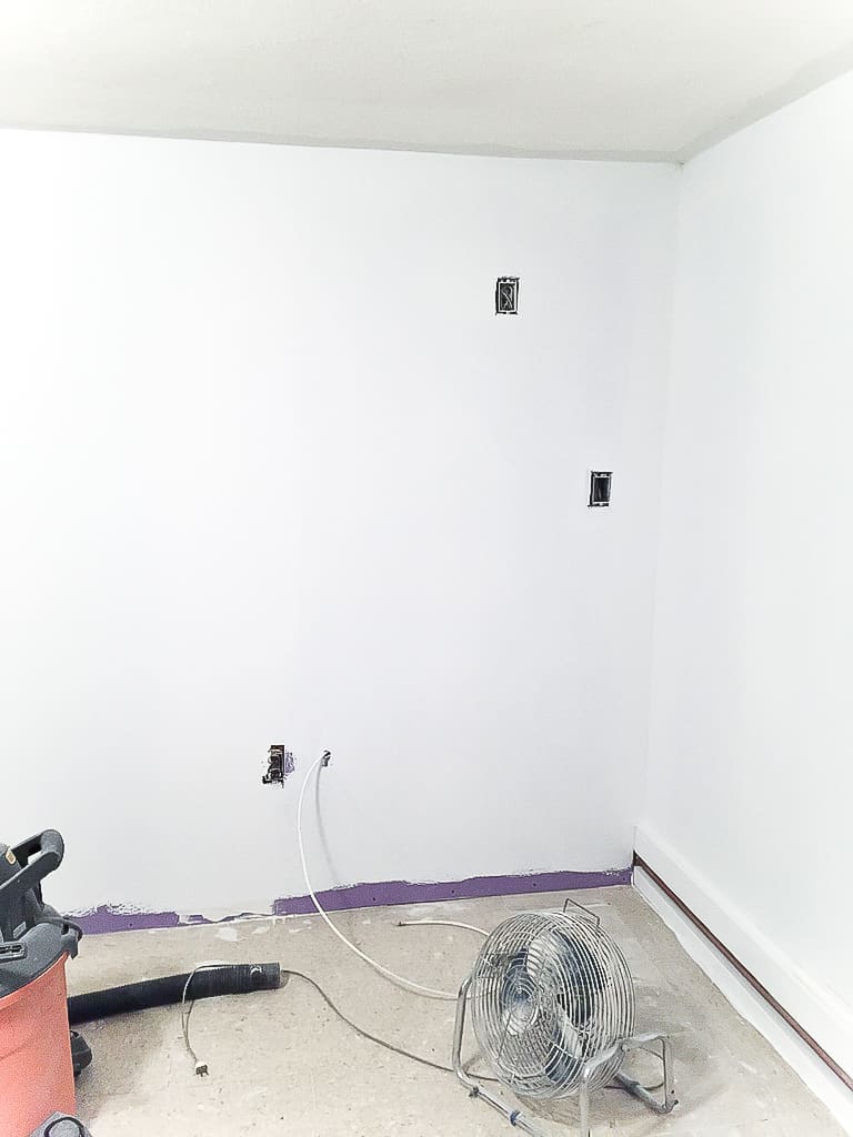 New drywall installed to replace old, wood paneling, and a fan and shop vac nearby