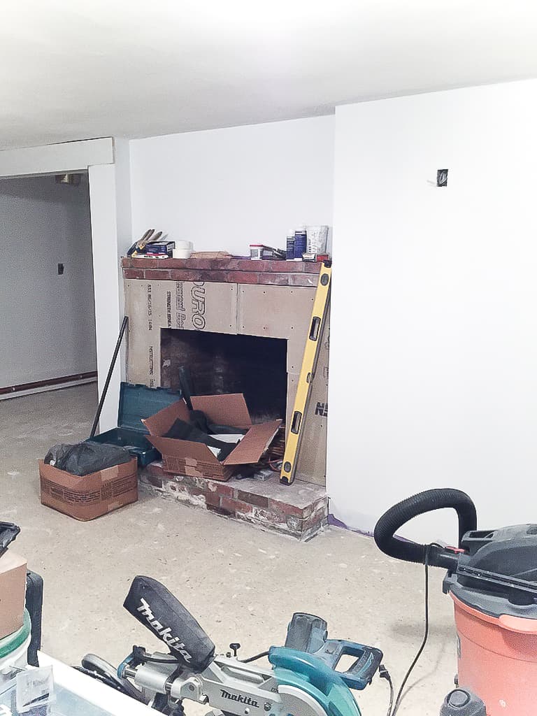 A fireplace surround with the brick covered in cement board, and numerous tools and materials nearby for work yet to be done