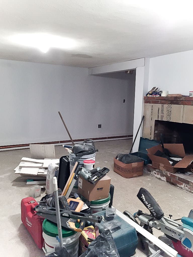 A messy room with various materials and power tools, near a fireplace with cement board installed and new drywall replacing wood paneling