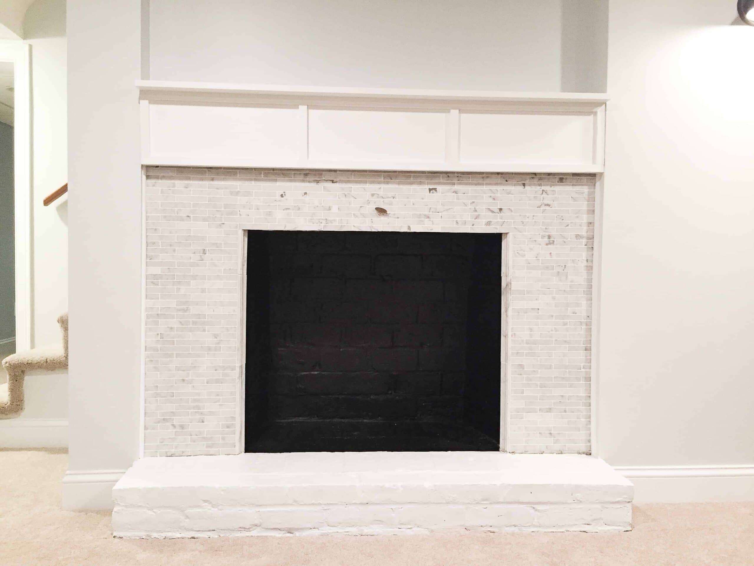 A basement fireplace with a white mantel, a tile surround and the firebox painted black, with a white painted stone hearth