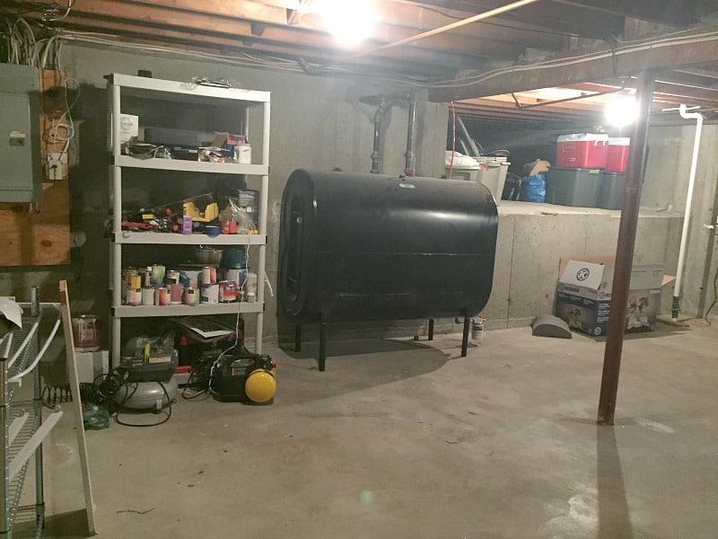 An unfinished section of the basement with concrete floors, an oil drum, a shelf with pantry items and various coolers in the background