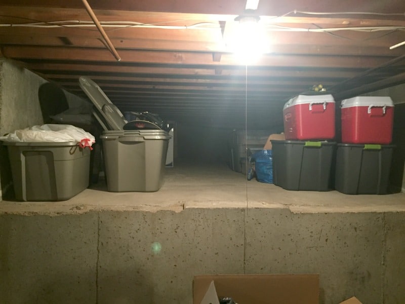 A collection of totes and coolers tucked into an alcove in the unfinished part of the basement, with an overhead light