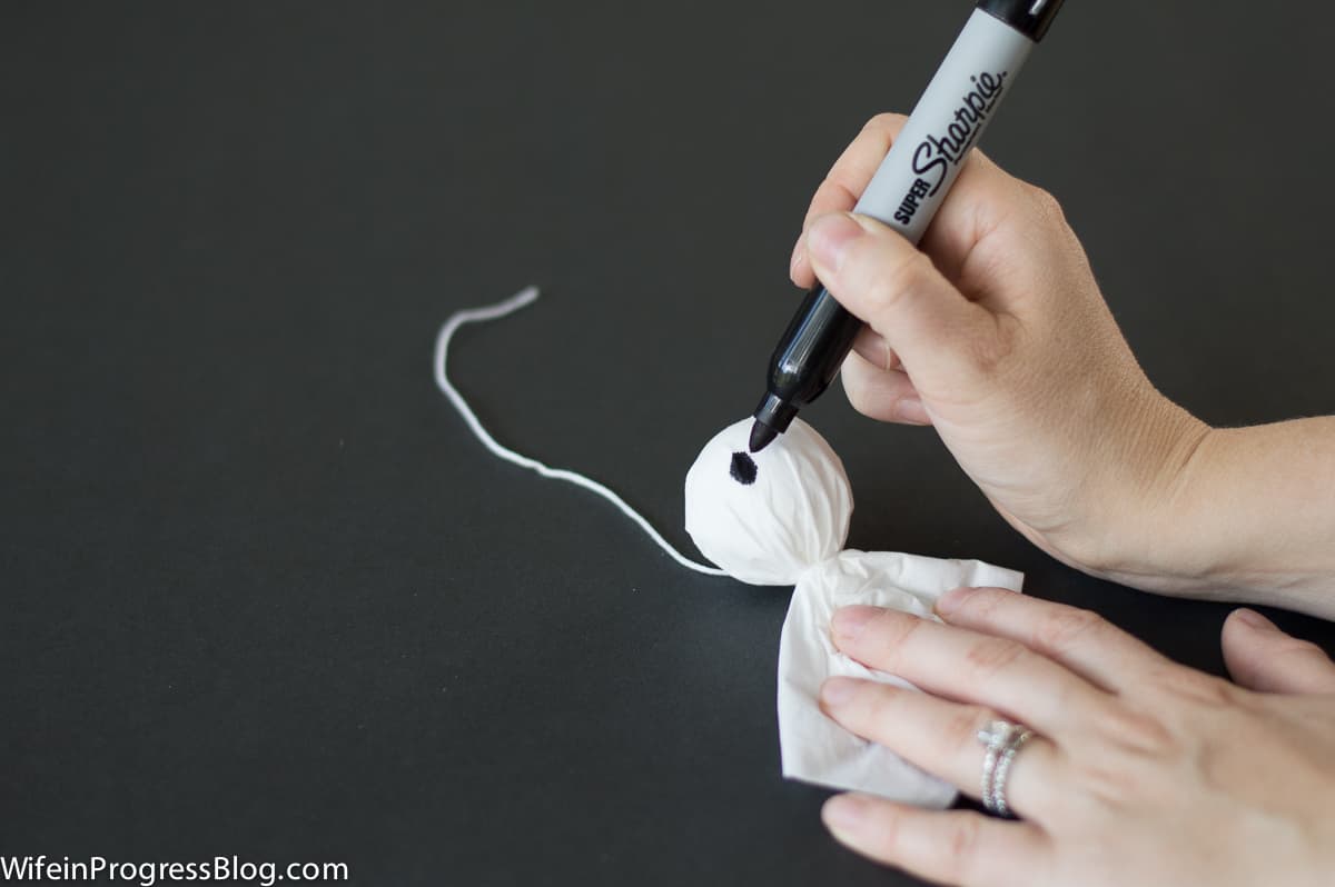 A person drawing eyes with a black permanent marker onto the face of a tissue ghost