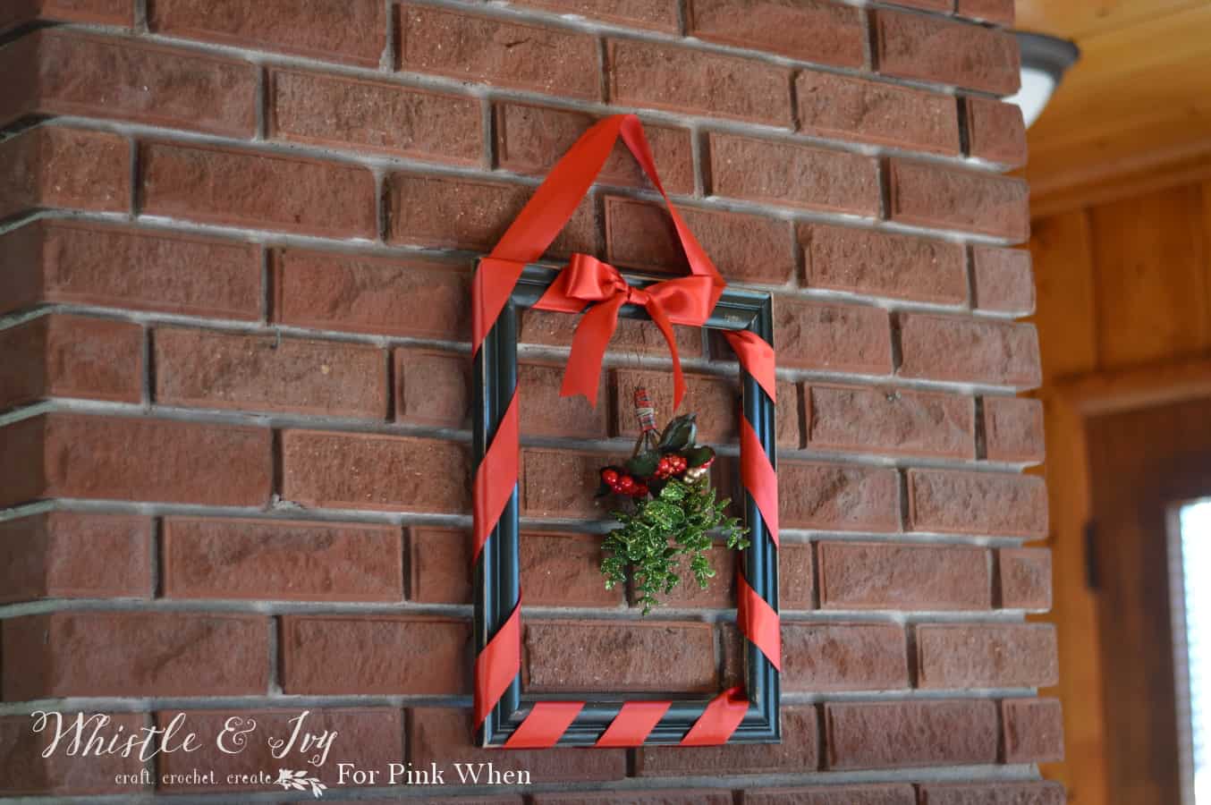 A square, dark photo frame without a back or glass insert, wrapped in red ribbon with a bunch of mistletoe hanging in the center