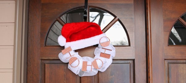 A front door with a wreath made from a Santa hat on top and a bunch of wide, white ribbon below with the words \'ho ho ho\' on the ribbon