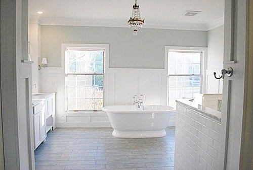 Sherwin Williams Sea Salt bathroom with wainscoting on lower half of the walls and a relaxing soaking tub in the middle of the room under a chandelier. 