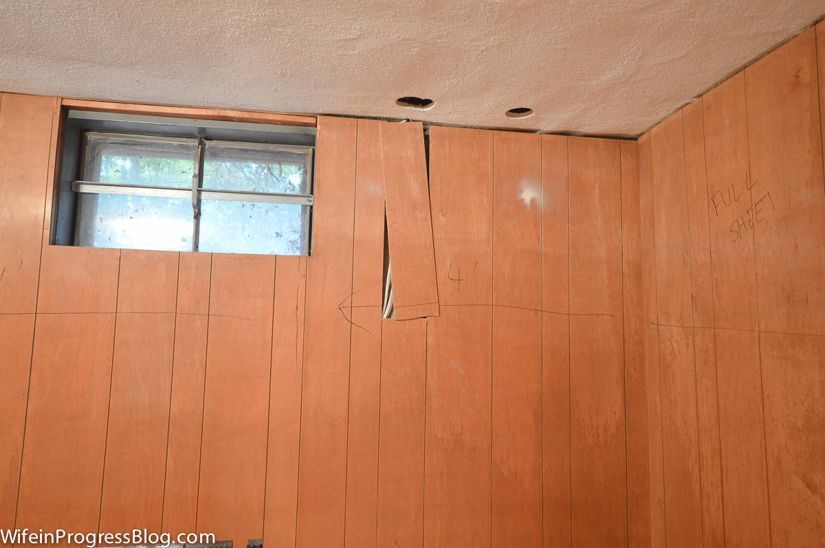 A window, wood paneling on the wall and two holes in the ceiling for more electrical wiring