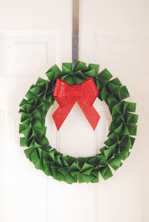 A circle of folded green paper and a red bow in the middle, hung from a front door