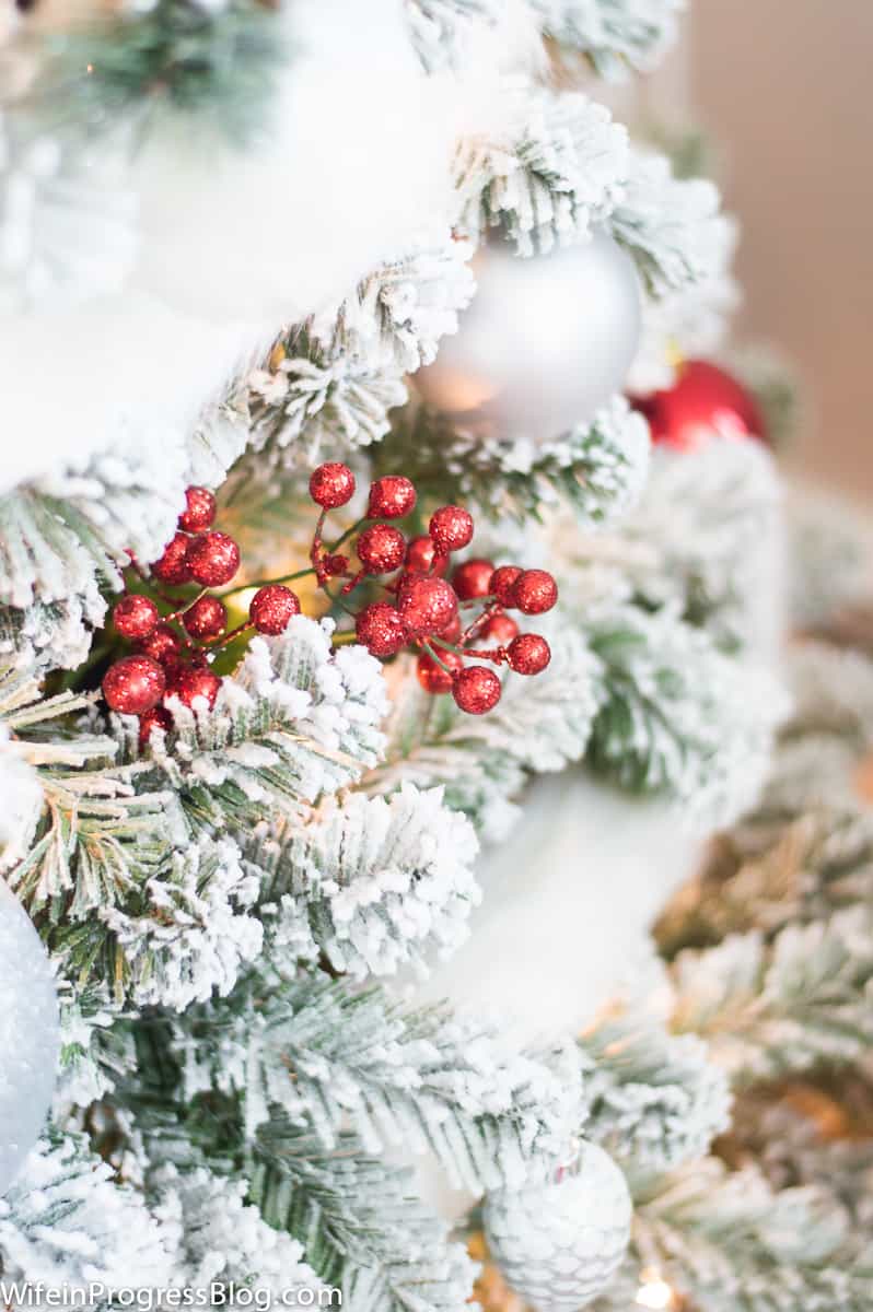 Berries tucked in among the branches of a white frosted artificial Christmas tree