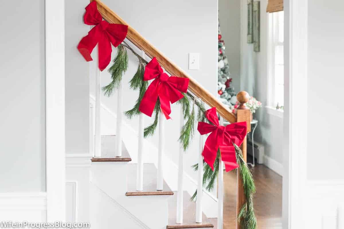 A staircase with large, red bows tied to pine branches on the railing