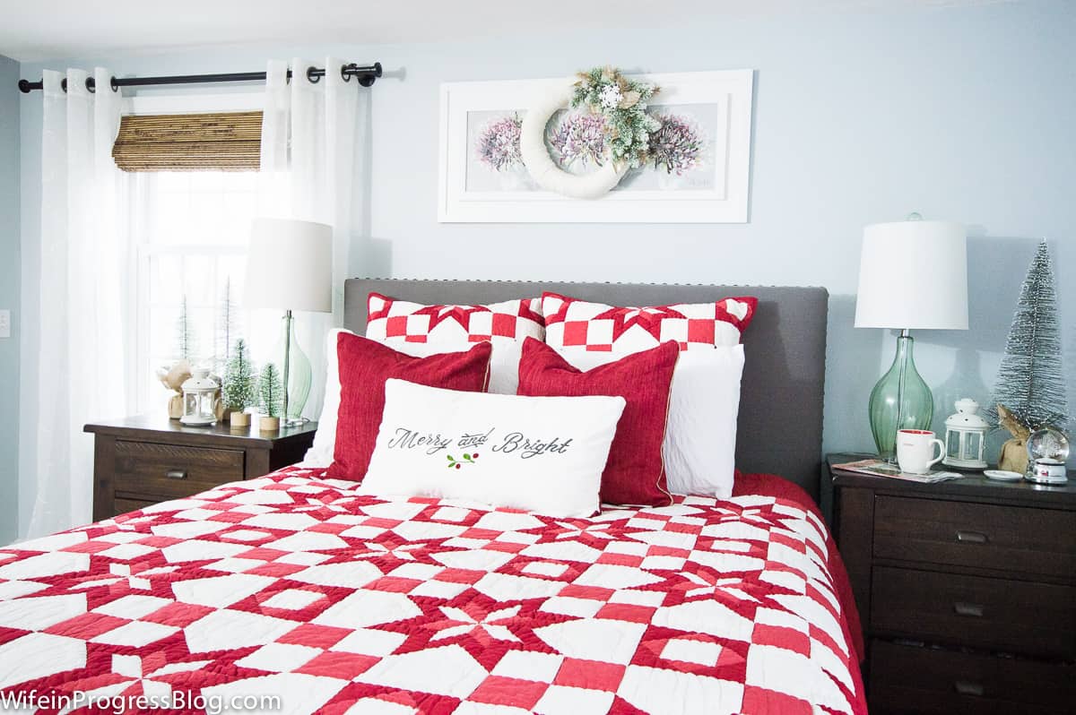 A bedroom with a red and white patterned quilt bedspread, matching pillows and solid white and red accessory pillows