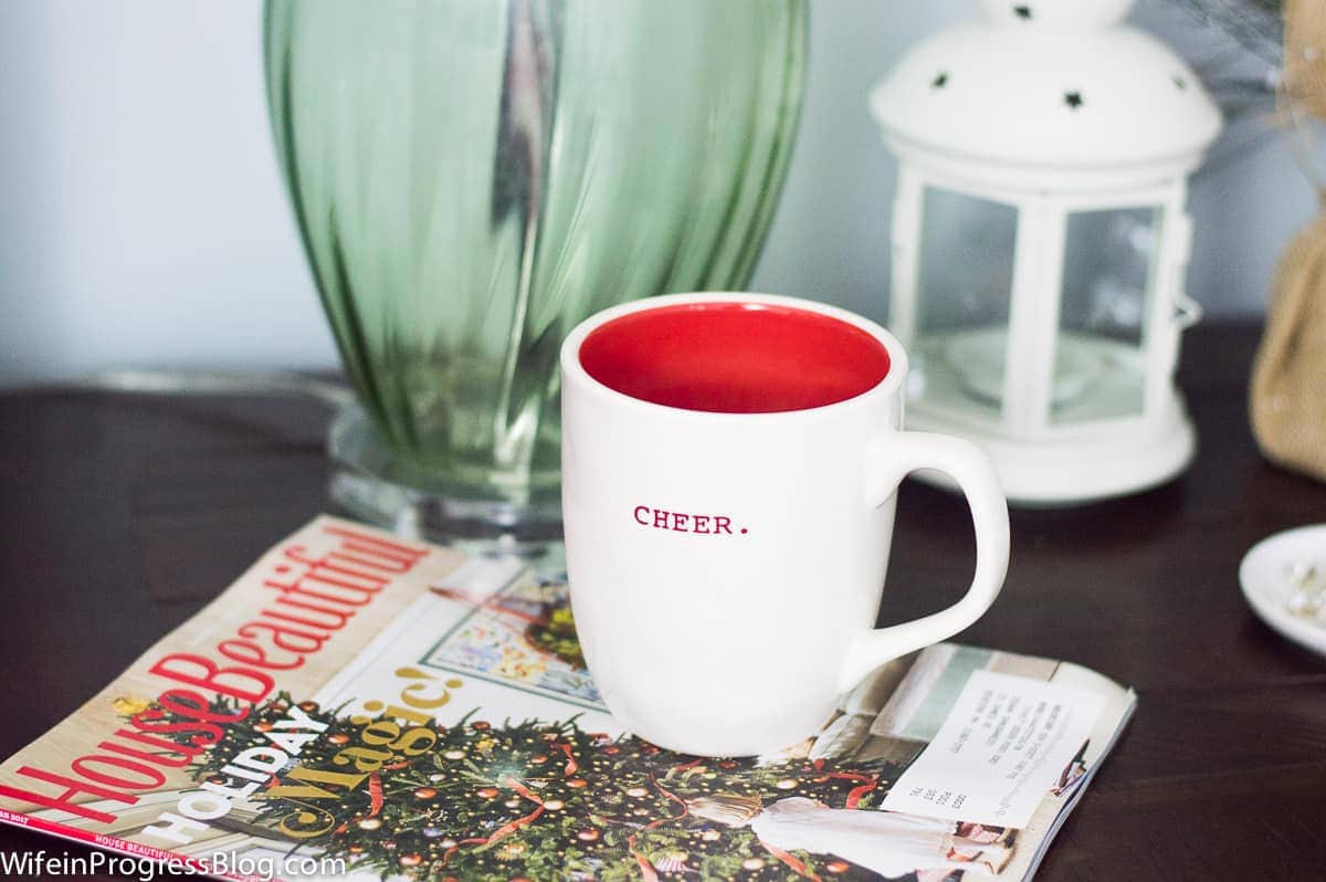 A white mug with a red interior, with the word \'cheer\' on the outside, resting on a magazine