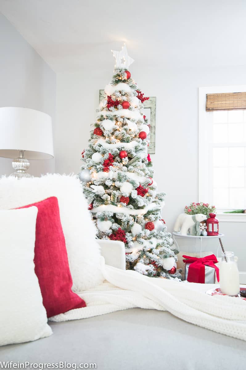 The corner of the Christmas tree, from the sofa, showing solid white and red throw pillows and a white blanket