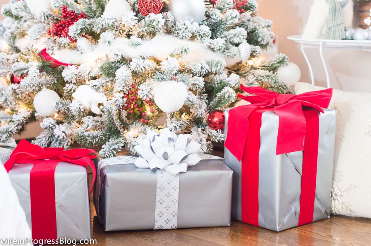Large presents under a Christmas tree, wrapped in solid grey paper and tied with wide white and red ribbons