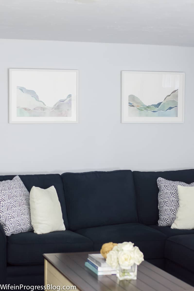 A navy sofa with blue and white throw pillows and two blue and white landscape paintings on the wall