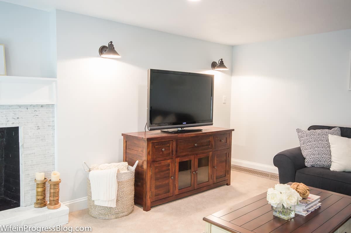 A tv on a wooden stand under two lights beside the fireplace in our newly remodeled basement.