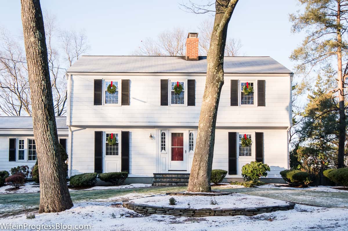 A two-story home with snow-covered lawn and a tall tree in front