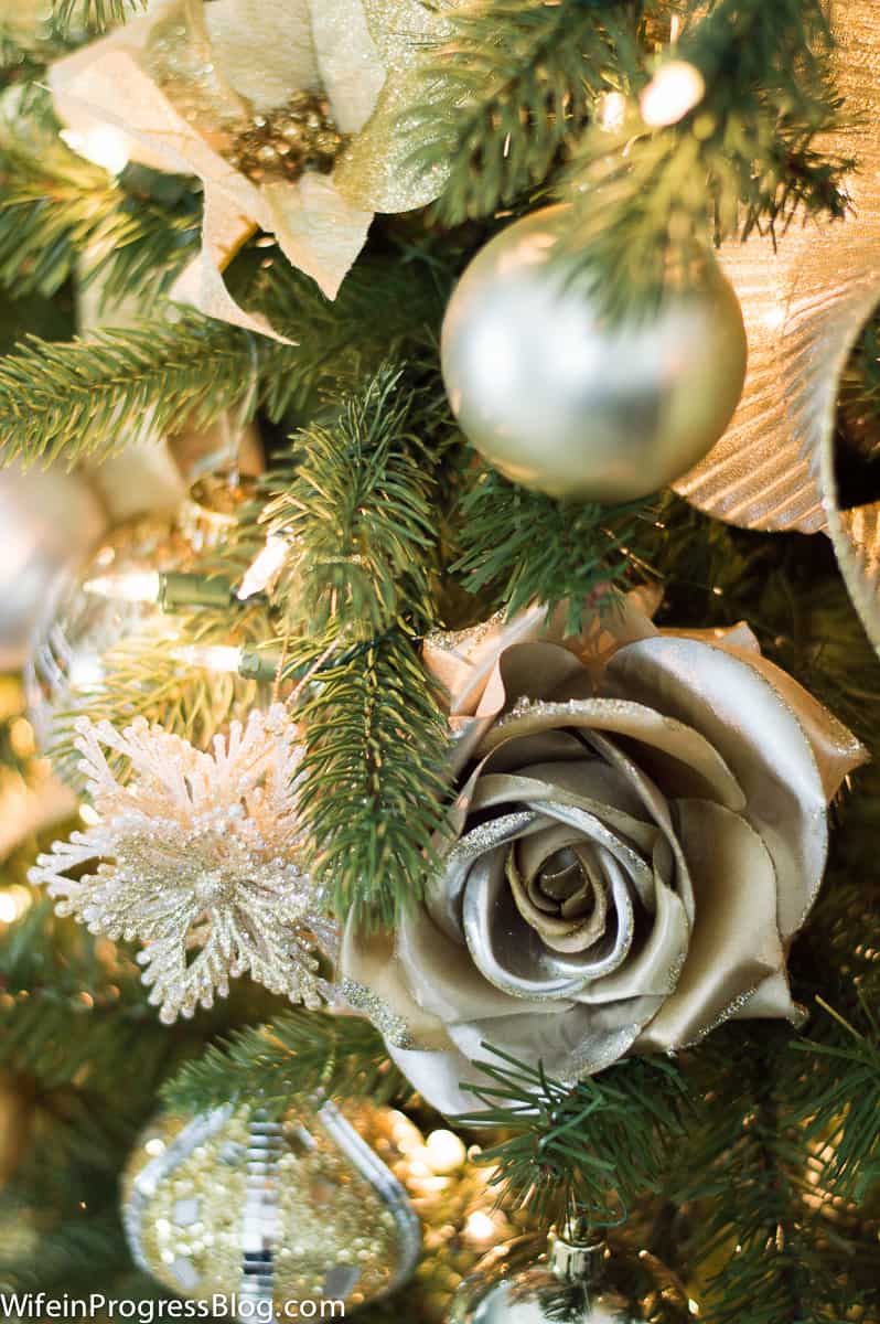 A close-up of gold and metallic flowers and ornaments on a lit Christmas tree