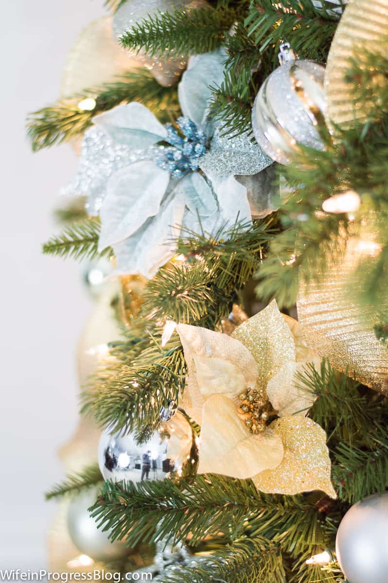 Gold and light blue poinsettia flowers on a lit Christmas tree with silver and gold ornament balls