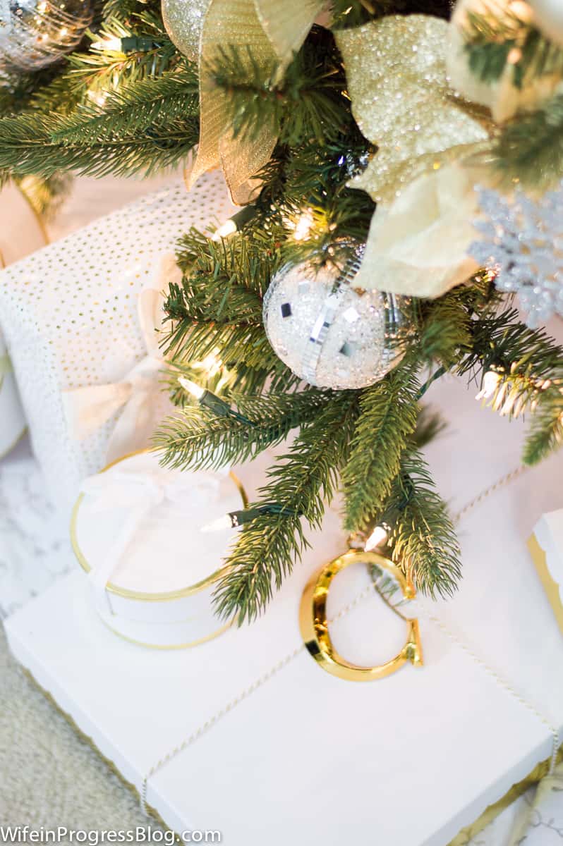 A close up of gifts wrapped in white and gold paper below the Christmas tree, embellished with golden initials for the recipients