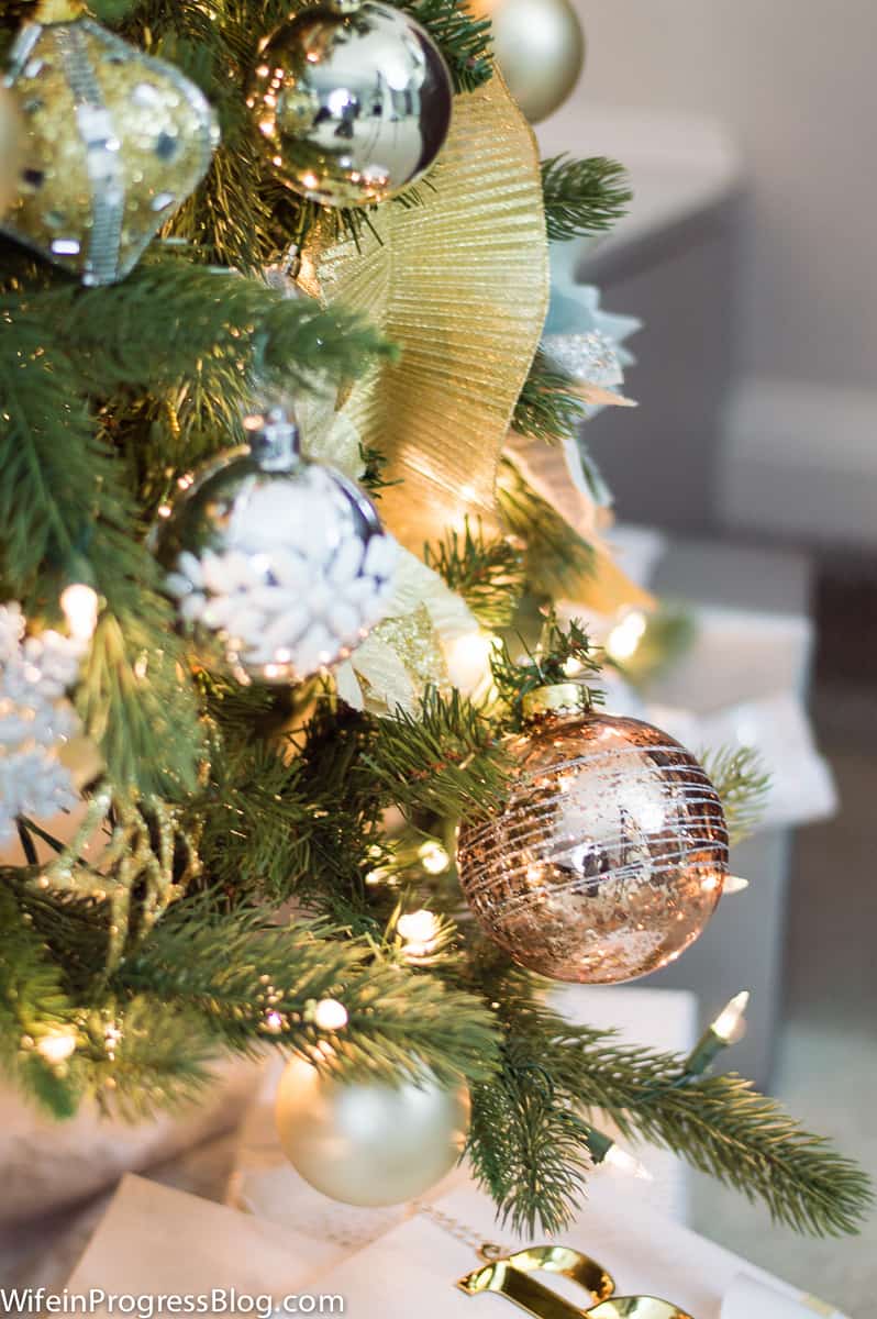 Gold, silver and copper ornament balls, white snowflakes and gold ribbon on a lit Christmas tree
